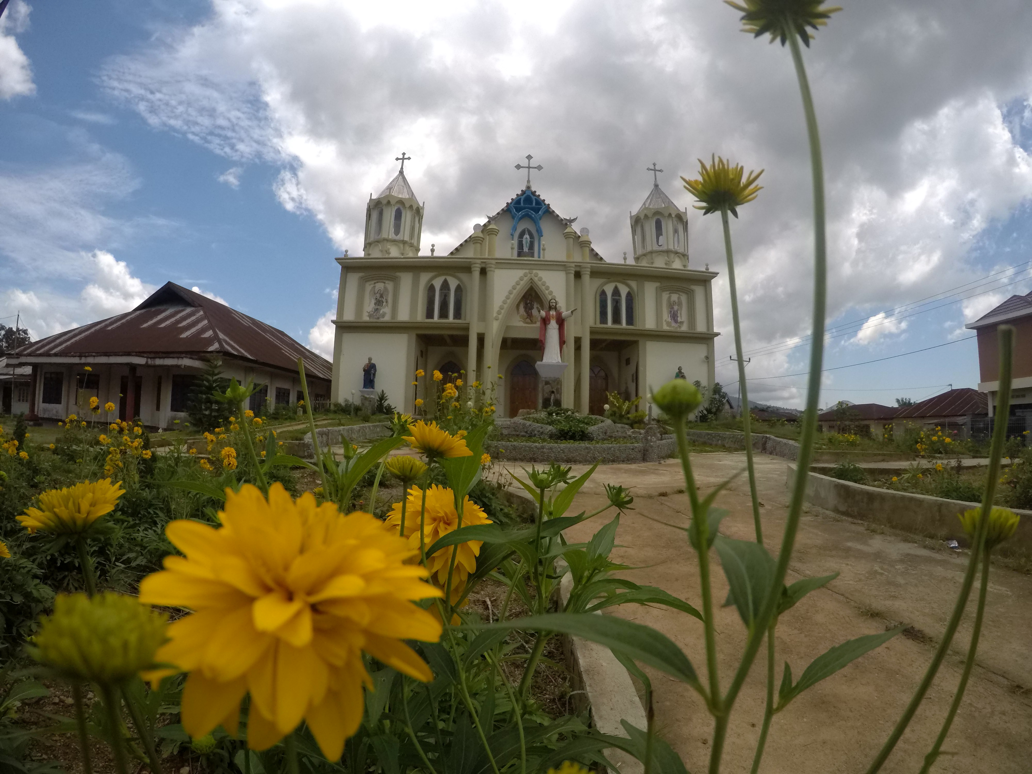 A huge church with bright yellow flowers in front of it and a large statue of Jesus.