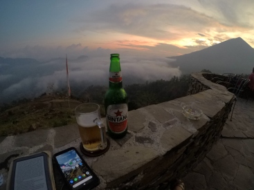 A kindle, phone and beer pictured with the volcano in the background.