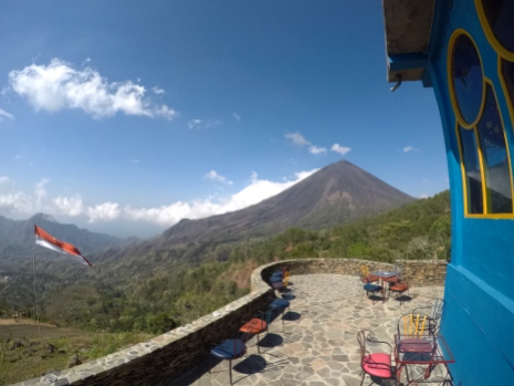 Tables and chairs from a restaurant in front of a volcano with the Indonesia flag alongside.