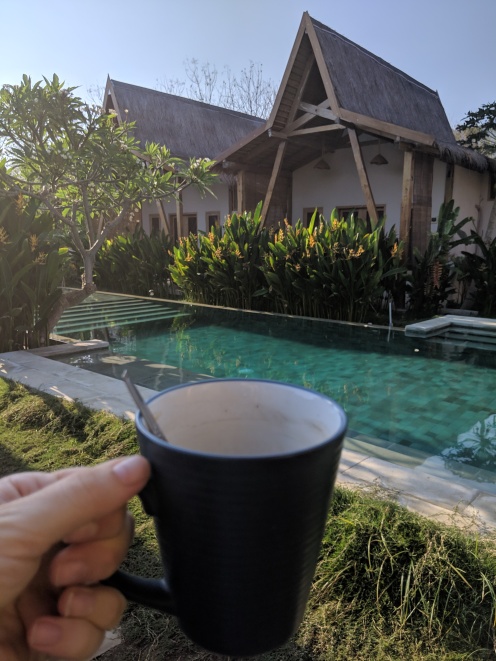 a cup of coffee held in front of a long swimming pool